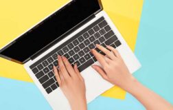 Hands on laptop keyboard with blue and yellow background